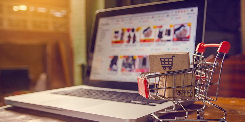 Image of laptop on desk next to miniature shopping cart